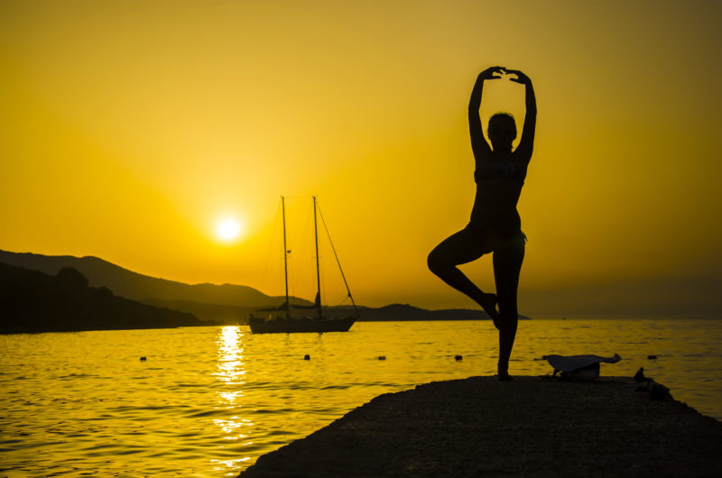 Silhouette of woman practicing yoga on the beach sunset