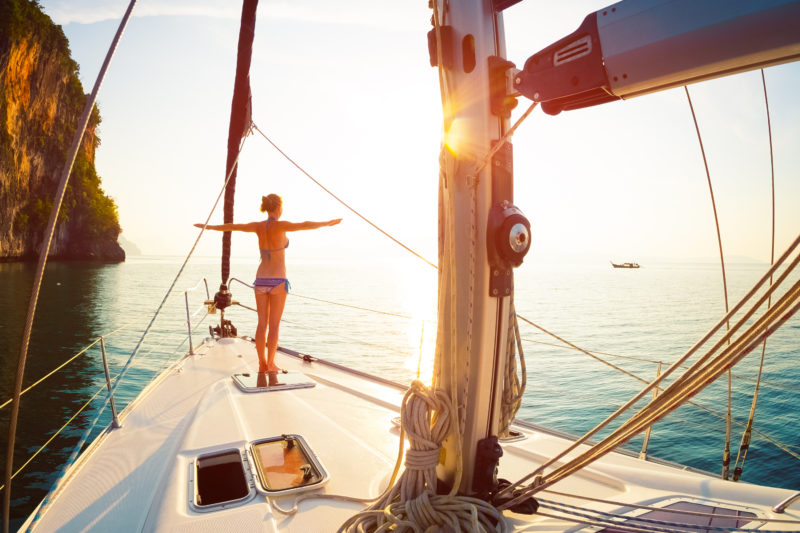 Young woman meets sunrise on the yacht anchored in the tropical sea